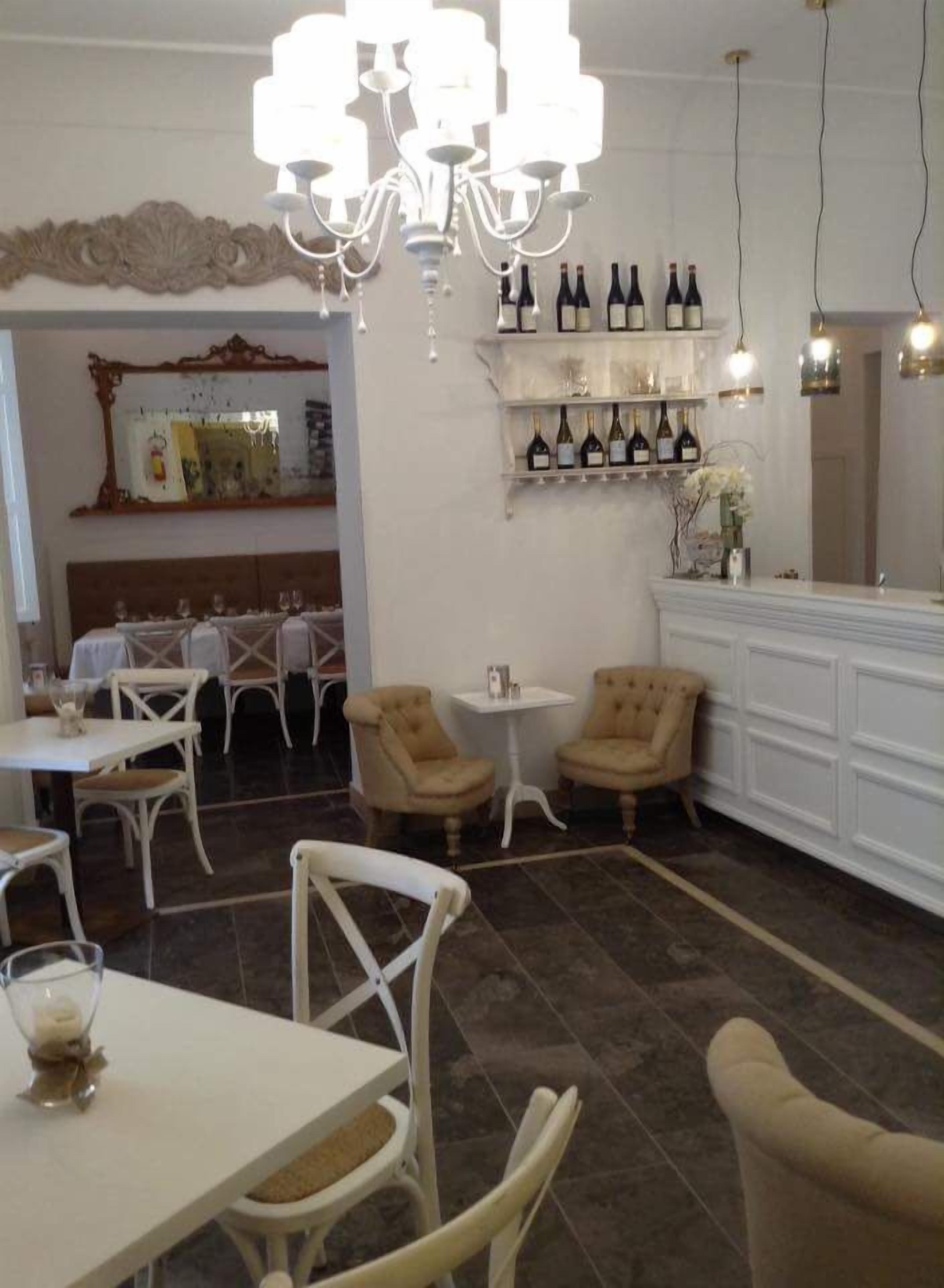 Un comedor con mobiliario blanco, una araña y botellas de vino en estanterías.