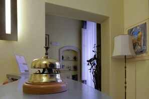 Zona de recepción de hotel con mostrador de madera, un timbre, escritorio con computadora y una lámpara.