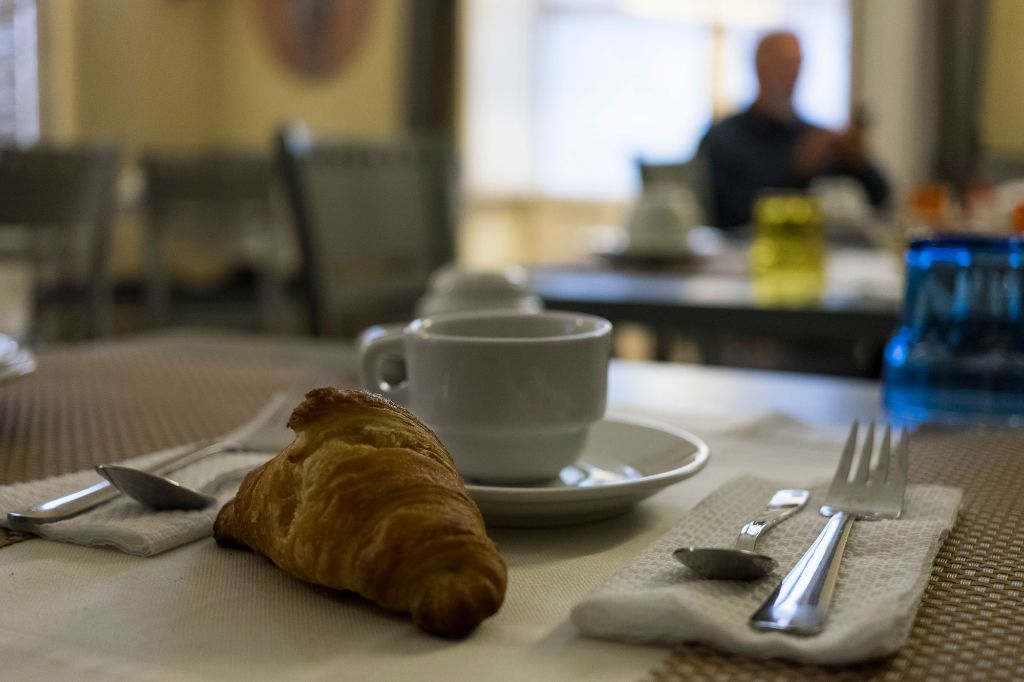 A breakfast setting with a croissant, a cup, and cutlery on a tablecloth.