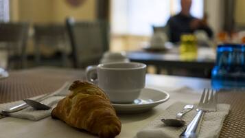 A breakfast setting with a croissant, a cup, and cutlery on a tablecloth.