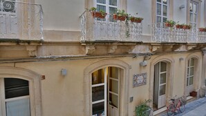 Un edificio con varias ventanas, un balcón con plantas en macetas y una bicicleta estacionada afuera.