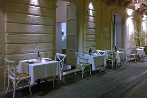 Un espace extérieur aménagé pour les repas, avec des tables et des chaises blanches, des murs en pierre et un sol pavé.