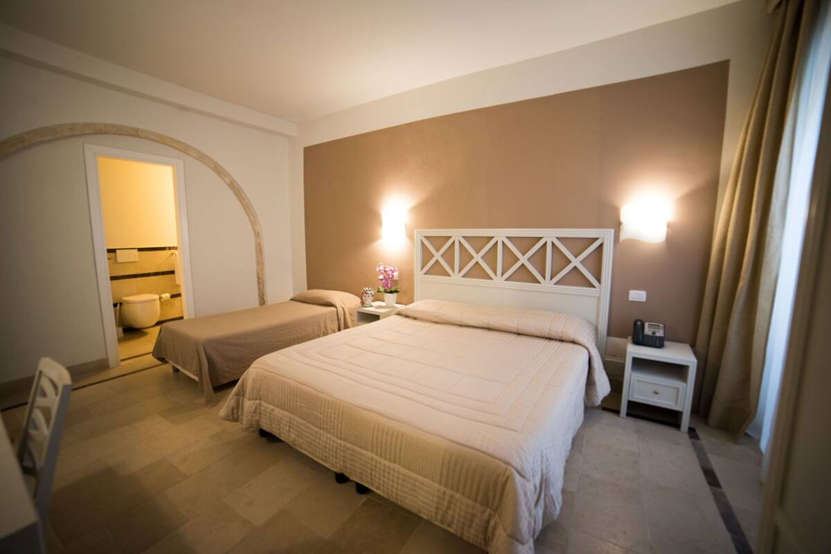 A hotel room with a large bed, a smaller bed, a nightstand with a phone, and a bathroom visible through an archway.