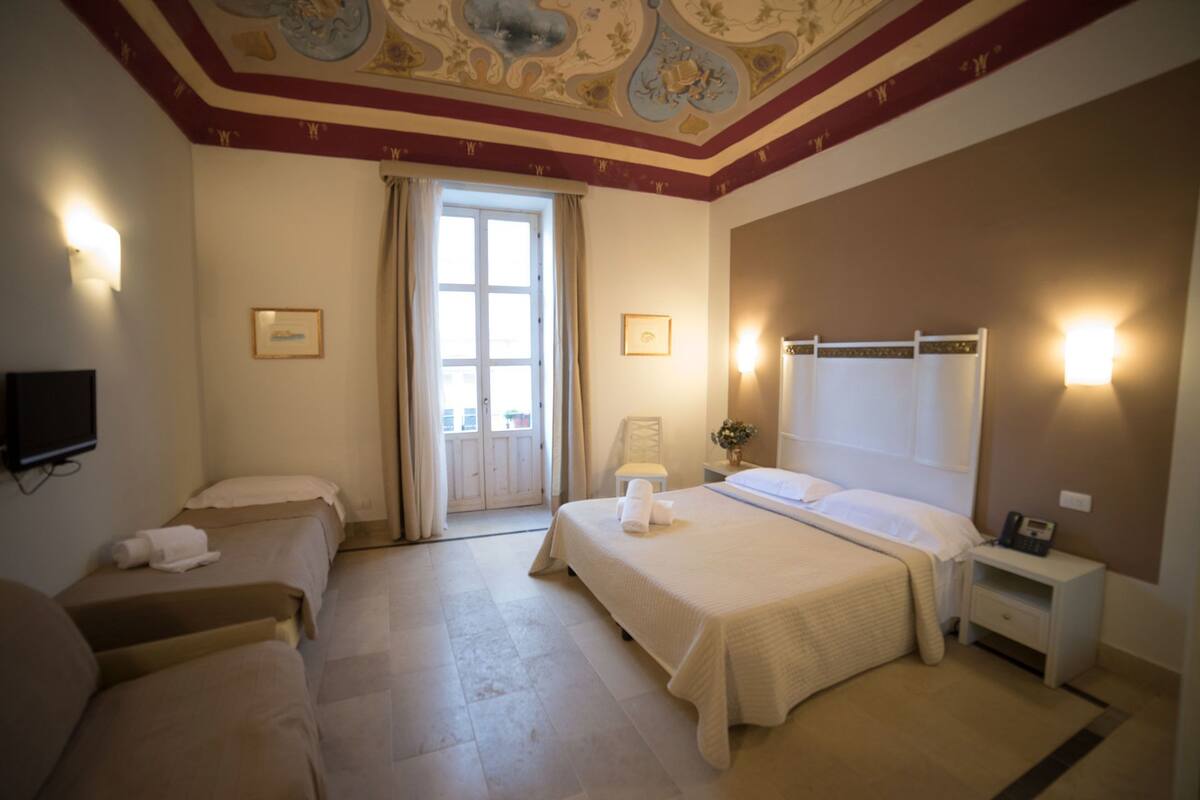 A hotel room with two beds, a television, a desk, and a large window.