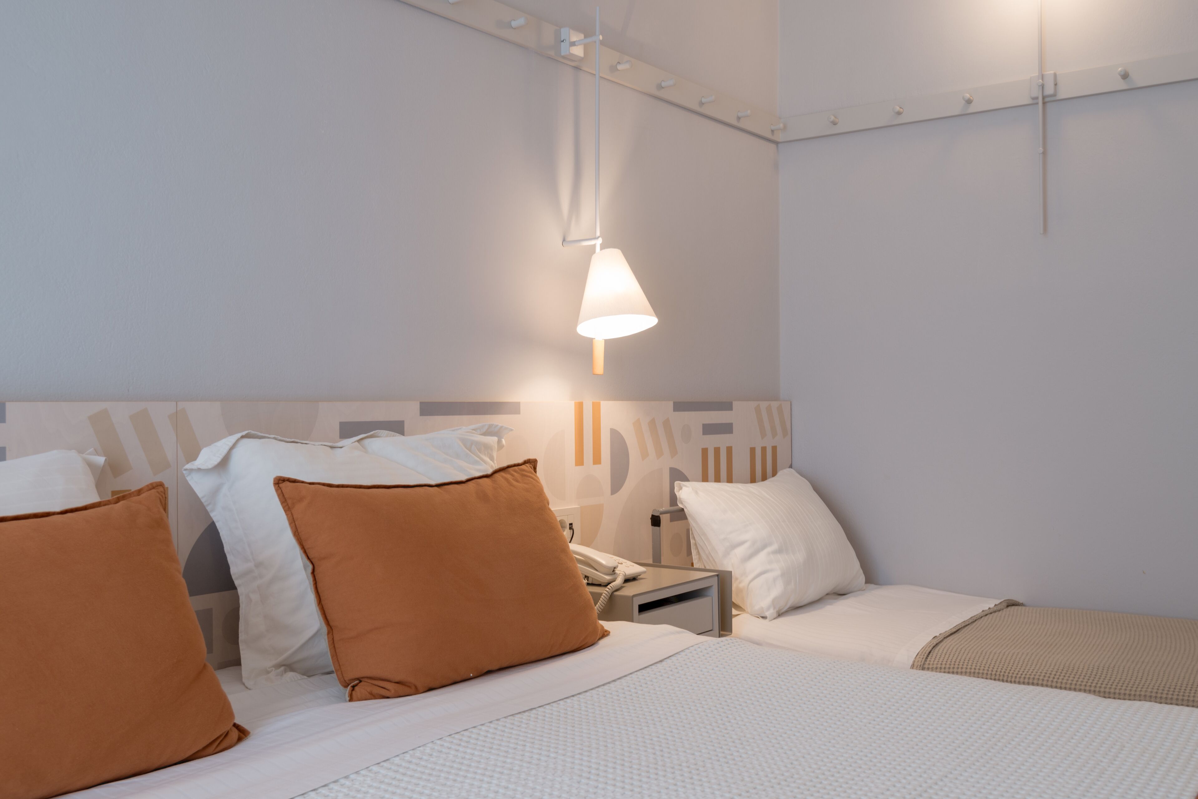 A hotel room with a bed, pillows, a bedside table with a lamp, and a wall-mounted telephone.