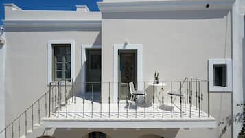 A white building with a balcony, a small table with chairs, and a potted plant.
