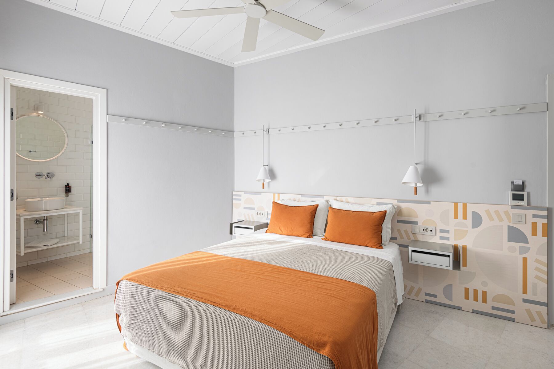 A modern bedroom with a bed, two bedside tables, a ceiling fan, and a bathroom visible through an open door.