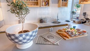 Une cuisine moderne avec des carreaux blancs, des étagères en bois, un grand saladier à carreaux et un coin repas avec du pain et des fruits.