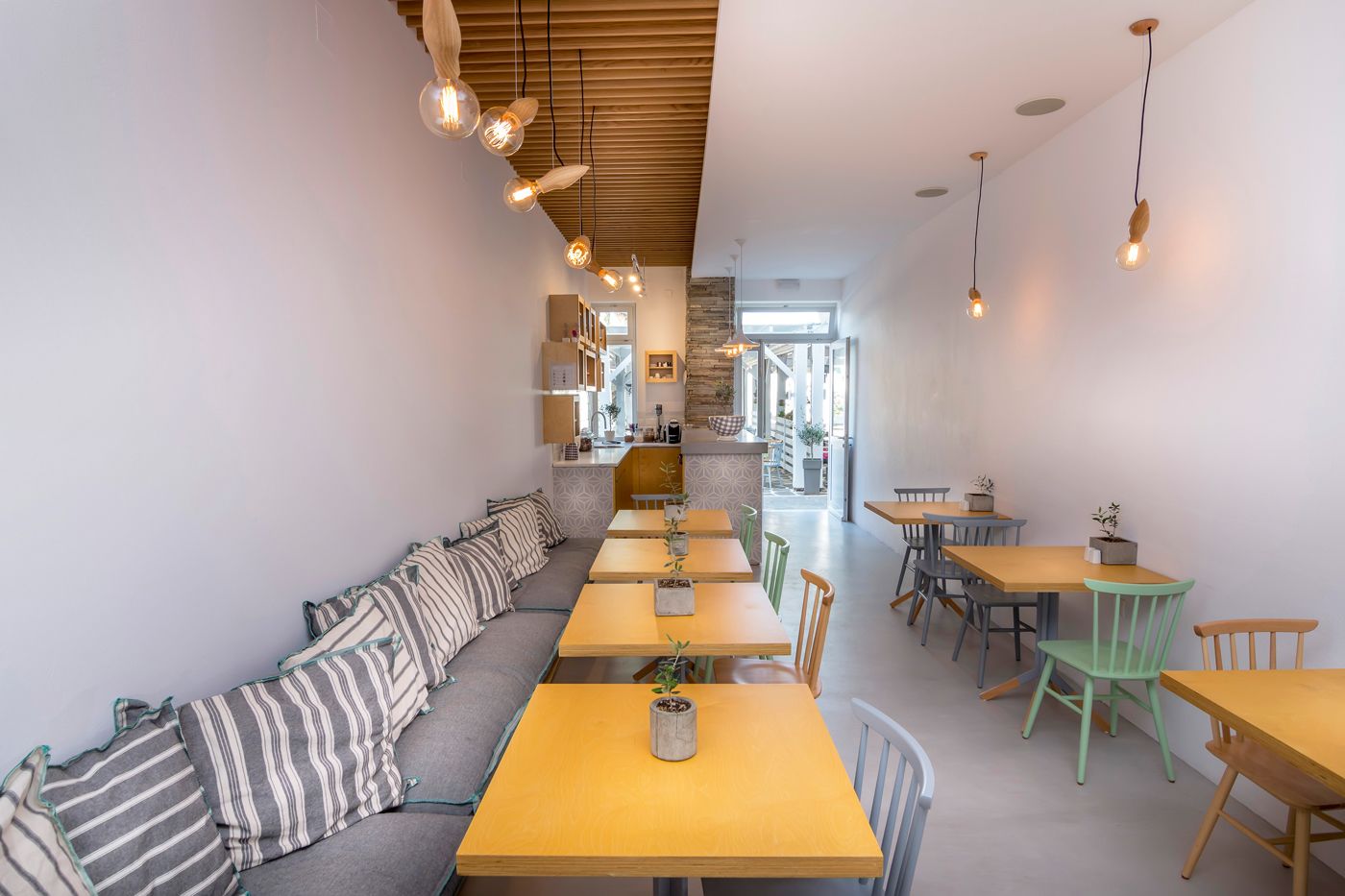 A modern interior with a long wooden bench, multiple tables, and hanging pendant lights.