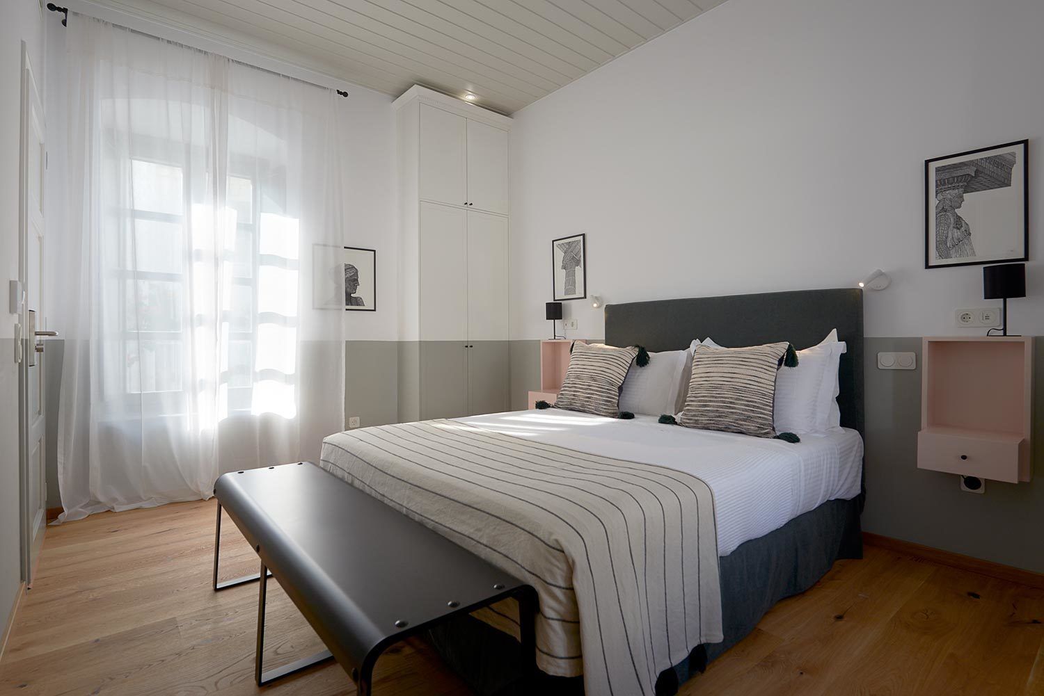 A bedroom with a bed, bench, bedside tables, and artwork on the walls.