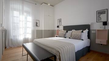 Un dormitorio con cama, banco, mesitas de noche y obras de arte en las paredes.