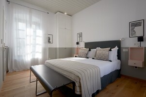 Un dormitorio con cama, banco, mesitas de noche y obras de arte en las paredes.