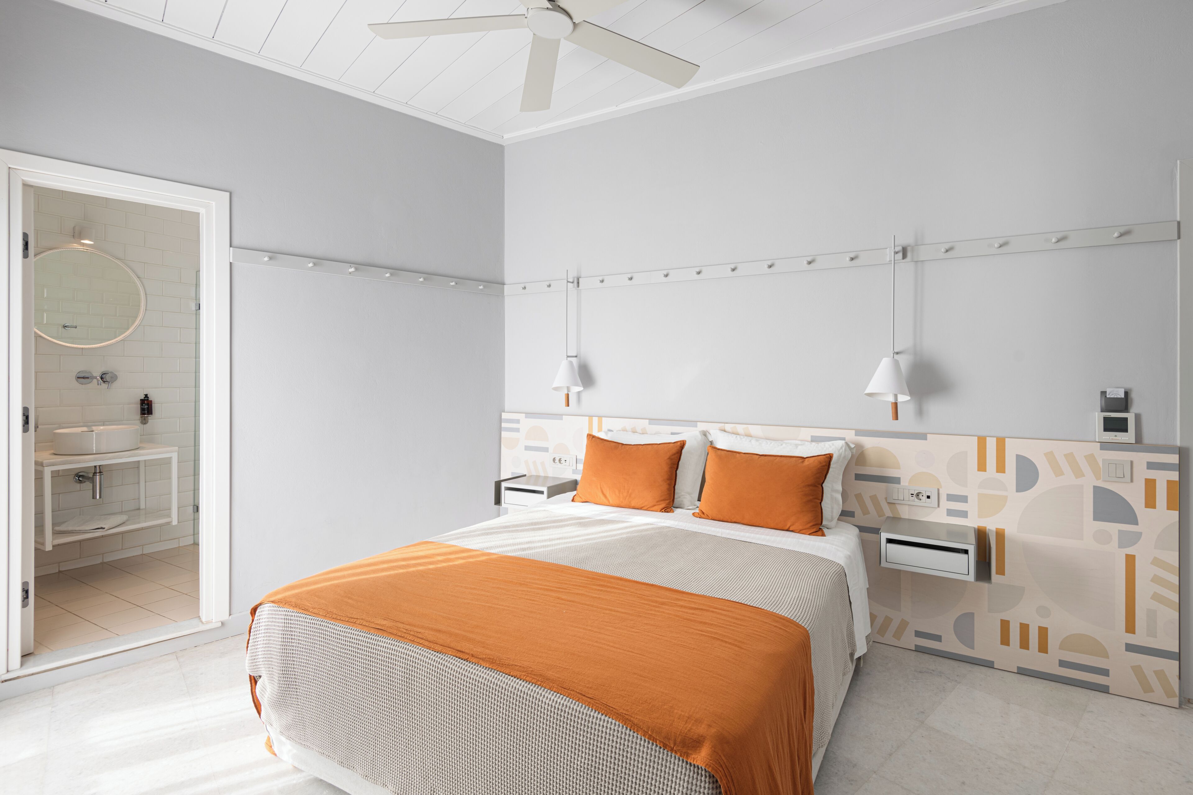 A modern hotel room with a bed, bedside tables, a ceiling fan, and a bathroom visible through an open door.