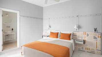 A modern hotel room with a bed, bedside tables, a ceiling fan, and a bathroom visible through an open door.