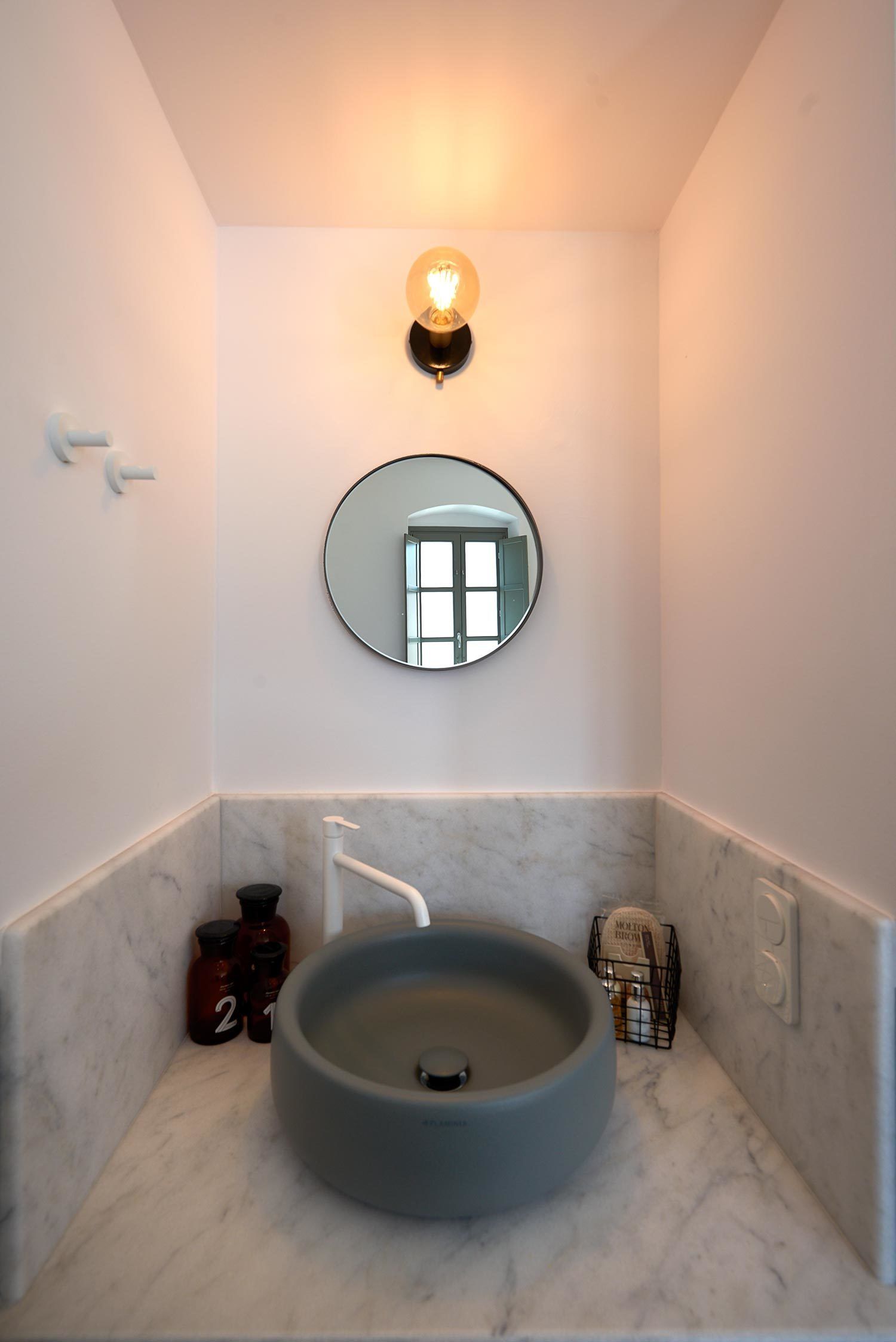 A bathroom with a round sink, a wall-mounted mirror, and a light fixture above the mirror.