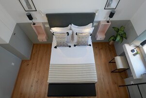 Un dormitorio moderno con una cama grande, lámparas de noche, una mesita de noche, una planta y vistas de la ciudad.