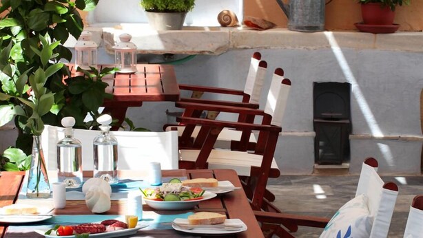 Un espace de restauration en plein air, avec des chaises en bois et une table dressée pour un repas, comprenant des assiettes de nourriture et des condiments.