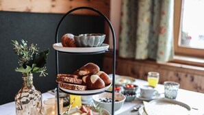 A breakfast setup with bread, cheese, and ham on a tiered stand, a vase with greenery, and a candle on a table. - Hotel Geisler Tulfes (Tulfes)