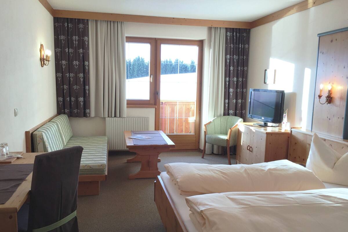 A hotel room with a bed, a desk with a chair, a television, a sofa, and a window with curtains.