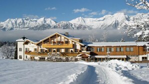 A large lodge with multiple buildings, a wooden facade, and a view of snow-covered mountains in the background. - Hotel Geisler Tulfes (Tulfes)