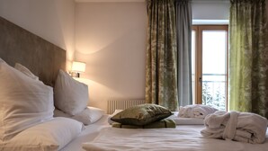 A hotel room with a neatly made bed, a bedside lamp, a window with curtains, and a radiator. - Hotel Geisler Tulfes (Tulfes)