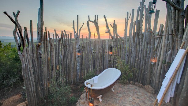 A rustic outdoor bathroom with a freestanding bathtub, surrounded by a wooden fence and stone flooring. - Garden Route Game Lodge (Albertinia)