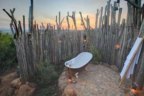 A rustic outdoor bathroom with a freestanding bathtub, surrounded by a wooden fence and stone flooring. - Garden Route Game Lodge (Albertinia)