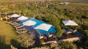 An aerial view of a resort with a swimming pool surrounded by lounge chairs and umbrellas, set in a lush, hilly landscape. - Garden Route Game Lodge (Albertinia)