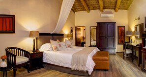 A bedroom with a bed, bedside tables, a chair, a desk, and a wardrobe. - Garden Route Game Lodge (Albertinia)
