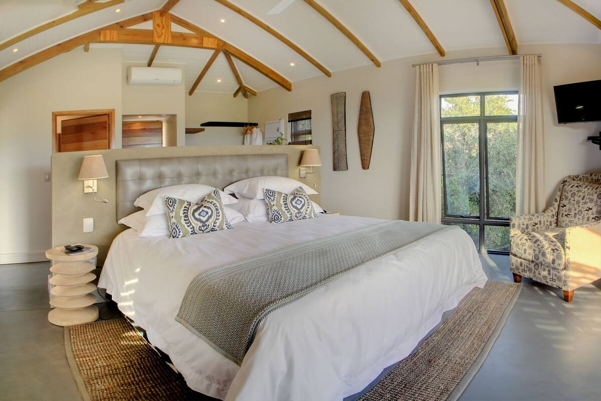 A spacious bedroom with a large bed, a TV, and a window with curtains.