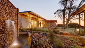 A modern building with a stone exterior, a wooden deck, and a landscaped garden with rocks and plants. - Garden Route Game Lodge (Albertinia)