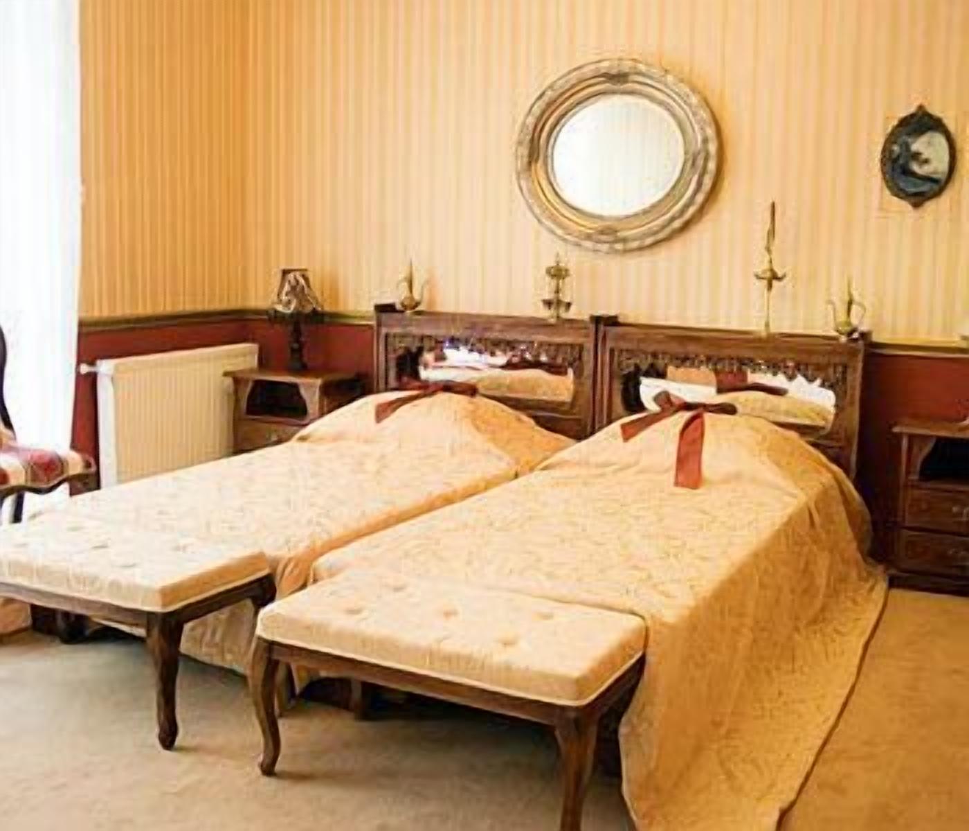 Ein Zimmer mit zwei Einzelbetten, einem runden Spiegel und einem kleinen Tisch mit einer Lampe.