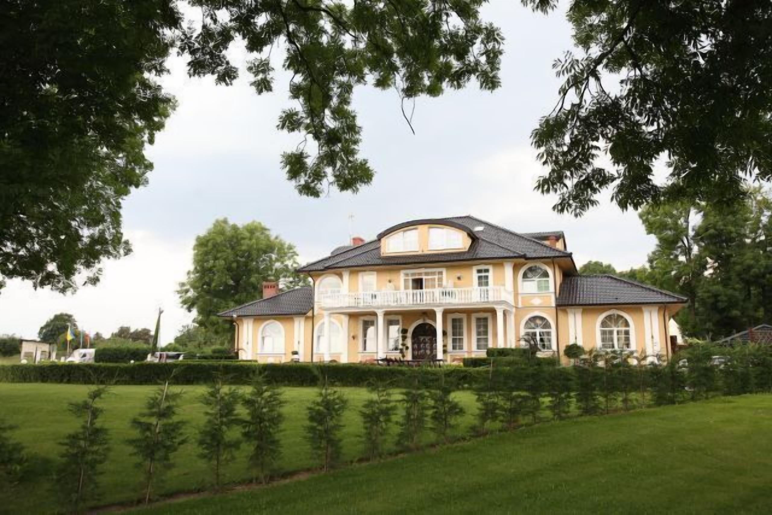 A large, two-story house with a balcony, surrounded by a well-maintained lawn and trees.