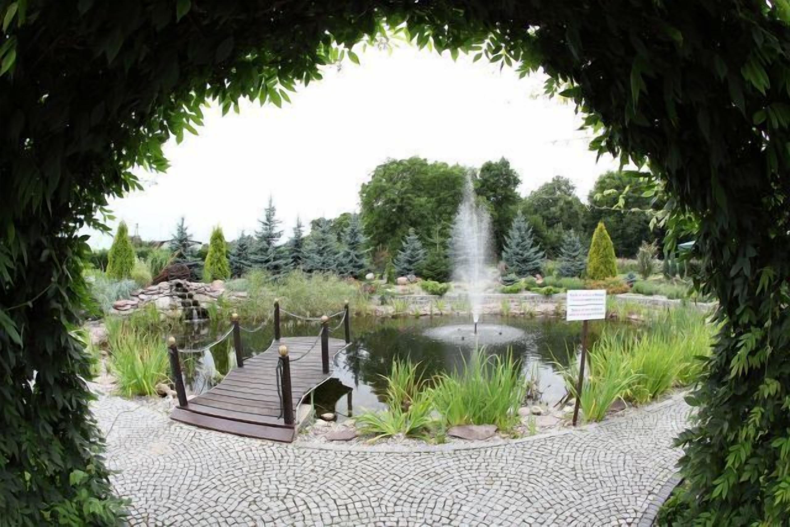 Ein Garten mit Teich, einer Holzbrücke und einem Schild.