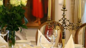 Een eettafel gedekt met een witte tafelkleed, borden, glazen en een kandelaar met kaarsen.