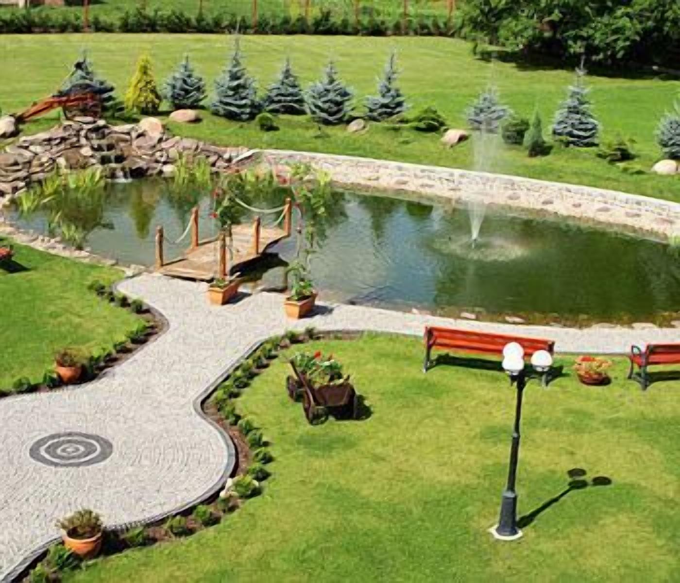 Ein angelegter Garten mit Teich, einer Holzbrücke und einem Weg.