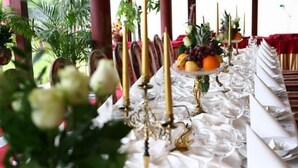 Een gedekte tafel met witte servetten, gouden kandelaars en een fruitmand.