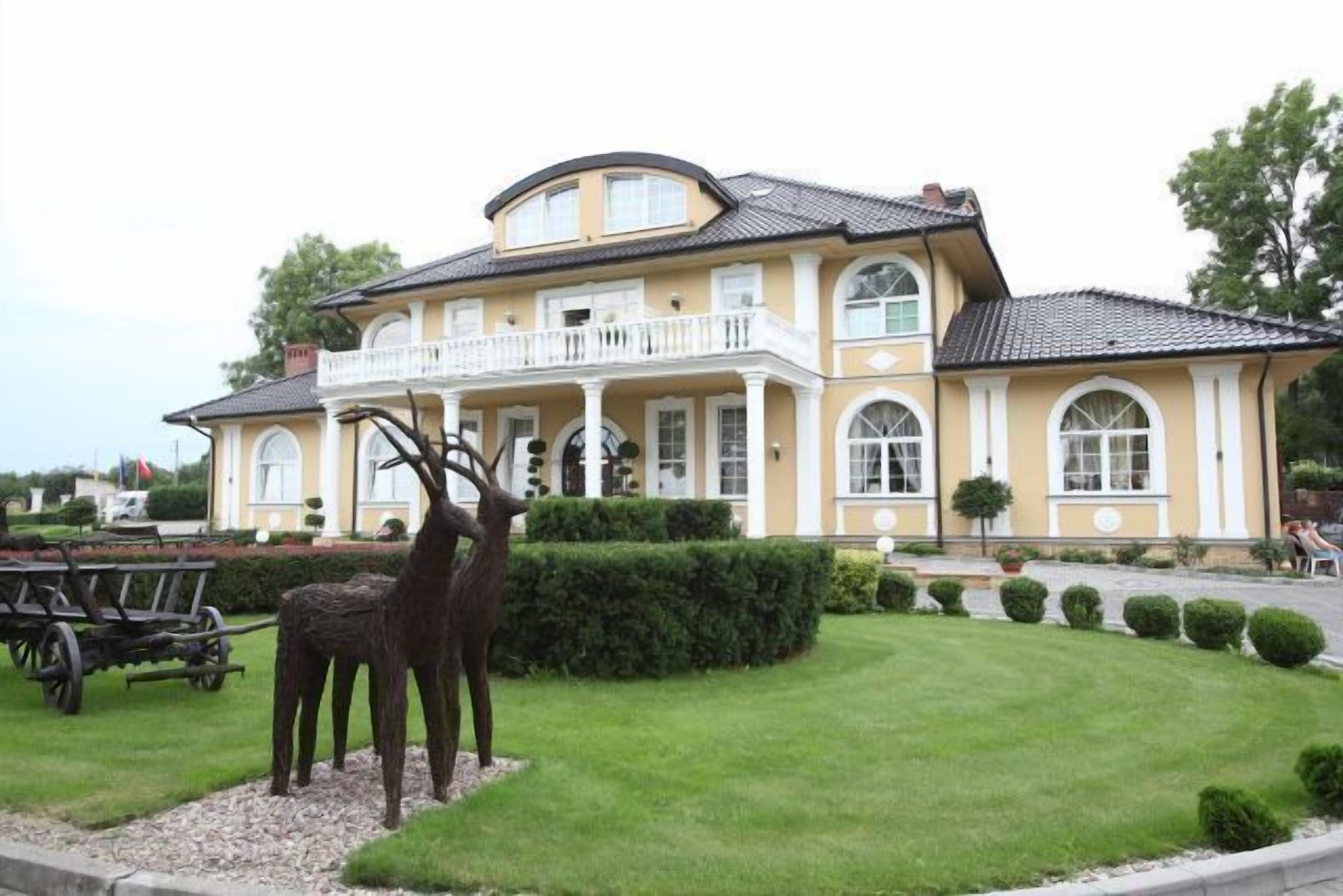 Un grand bâtiment jaune doté d’un balcon, entouré d’une pelouse bien entretenue et orné d’une sculpture de cerfs.