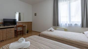 Habitación de hotel con dos camas, un escritorio con televisor, una silla y una ventana con cortinas.