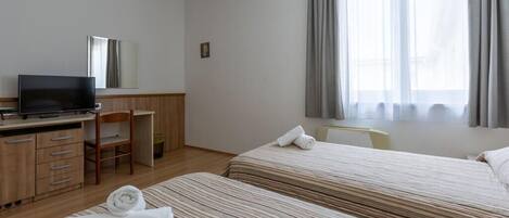 A hotel room with two beds, a desk with a television, a chair, and a window with curtains.