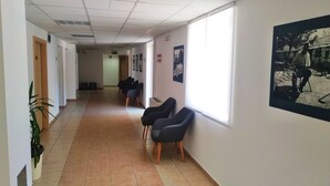 A hallway with chairs lined up against the wall, a tiled floor, and a large window on the right. - Hotel Porto (Zadar)
