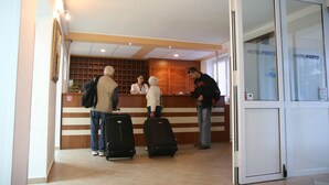 A hotel reception area with a wooden reception desk, a glass door, and a tiled floor. - Hotel Porto (Zadar)