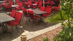 An outdoor seating area with red chairs and white umbrellas, arranged on a paved patio. - Hotel Porto (Zadar)