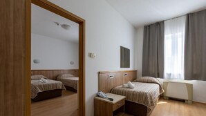 A hotel room with two beds, a wooden floor, a bedside table with a phone, a radiator, and a window with curtains. - Hotel Porto (Zadar)