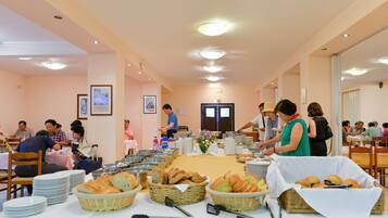 Un buffet avec plusieurs points de service, des tables et des paniers remplis de pain et d’autres aliments.