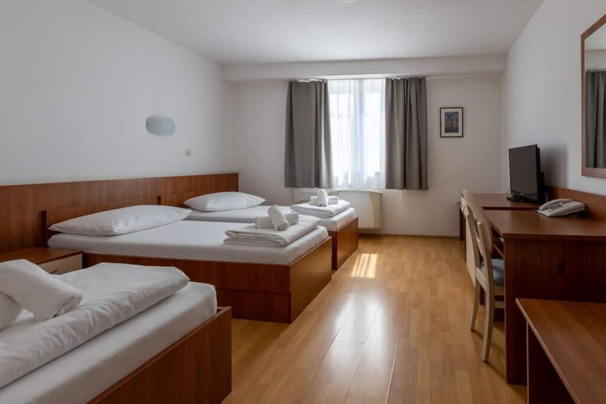 Une chambre d’hôtel avec deux lits simples, un bureau avec une chaise, une télévision et une fenêtre avec des rideaux.