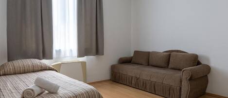 A room with a bed, a sofa, and a window with curtains.