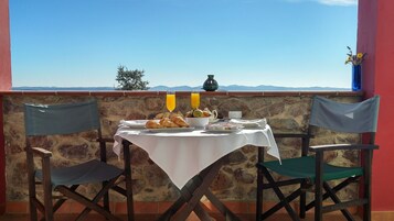 A table set with croissants, fruit, and juice glasses, overlooking a mountainous landscape.
