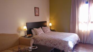 A hotel room with a bed, a sofa, a nightstand with a lamp, and a framed picture on the wall.