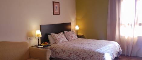 Habitación de hotel con cama, sofá, mesita de noche con lámpara y un cuadro en la pared.